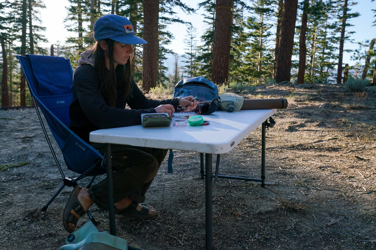 A person sits at a folding table with fishing line and equipment on the table top.