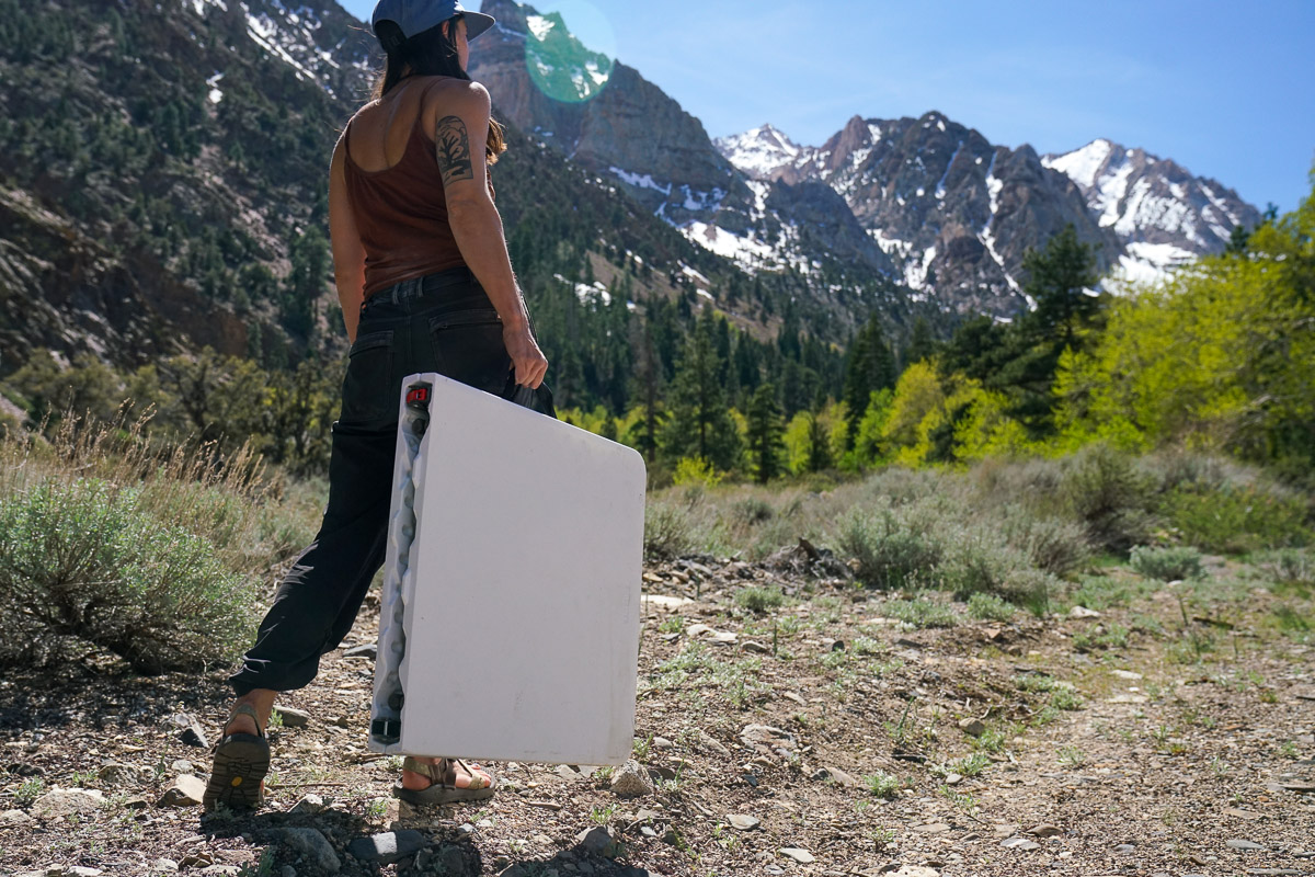 A person walks away from the camera holding a folding table in hand. There are mountains in the background.