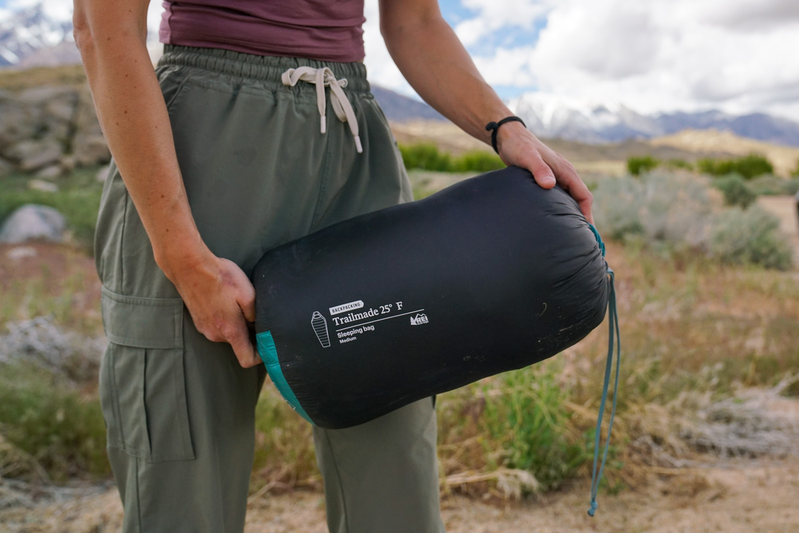 A close up of a sleeping bag enclosed in a stuff sack. A person holds the bag.