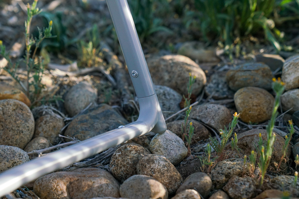 A close up of a single foot of a camping chair. The foot rests on rocky terrain.