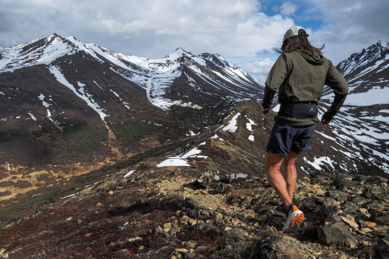 Person standing on a rocky ridge overlooking snow-capped mountains.