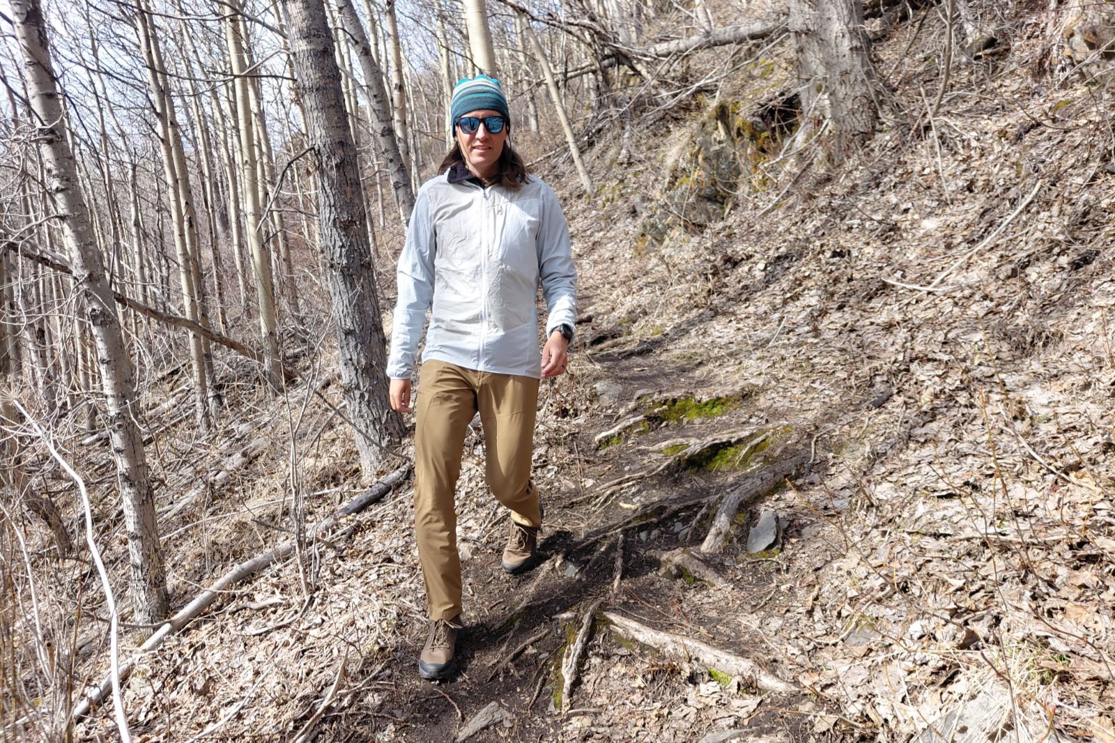 Person walking on a dirt trail in a leafless forest wearing outdoor gear.