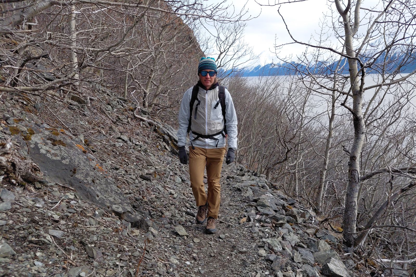 Person hiking on a rocky trail with leafless trees and distant mountains in the background.