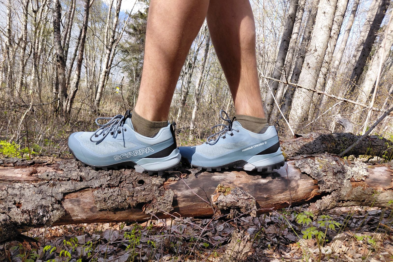 Person wearing light blue hiking shoes walking on a log in a forest.