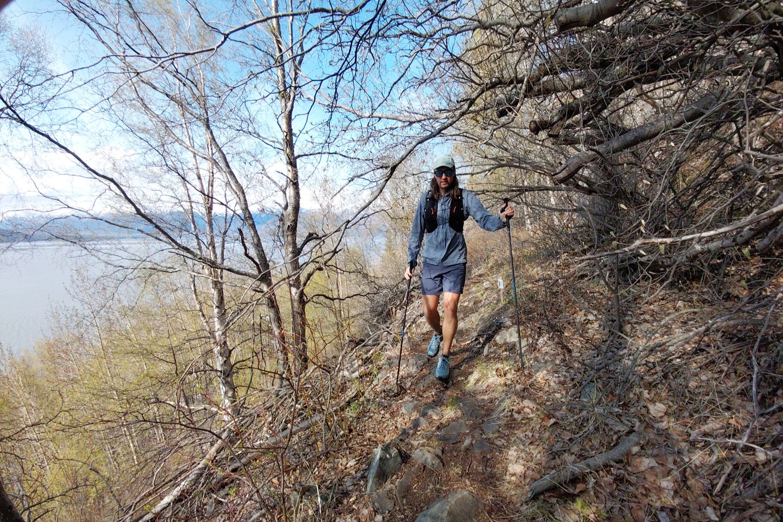 A hiker walks along a scenic trail with expansive views of a body of water and distant mountains.