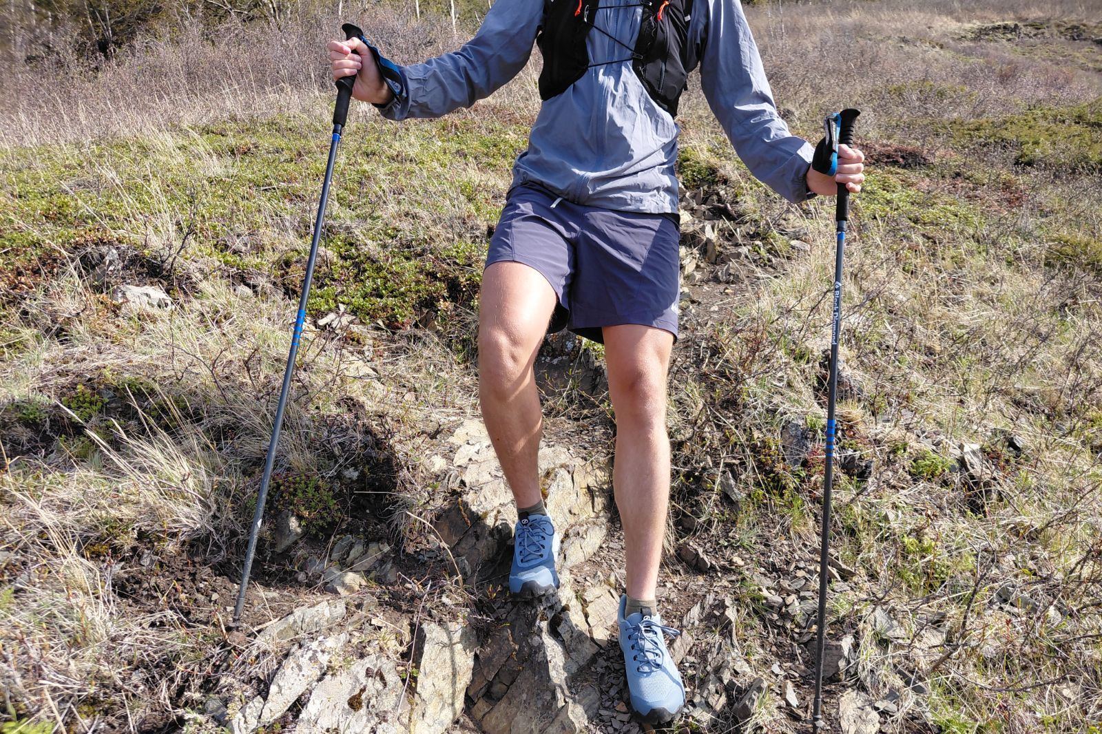 A person uses trekking poles while hiking a rugged trail.