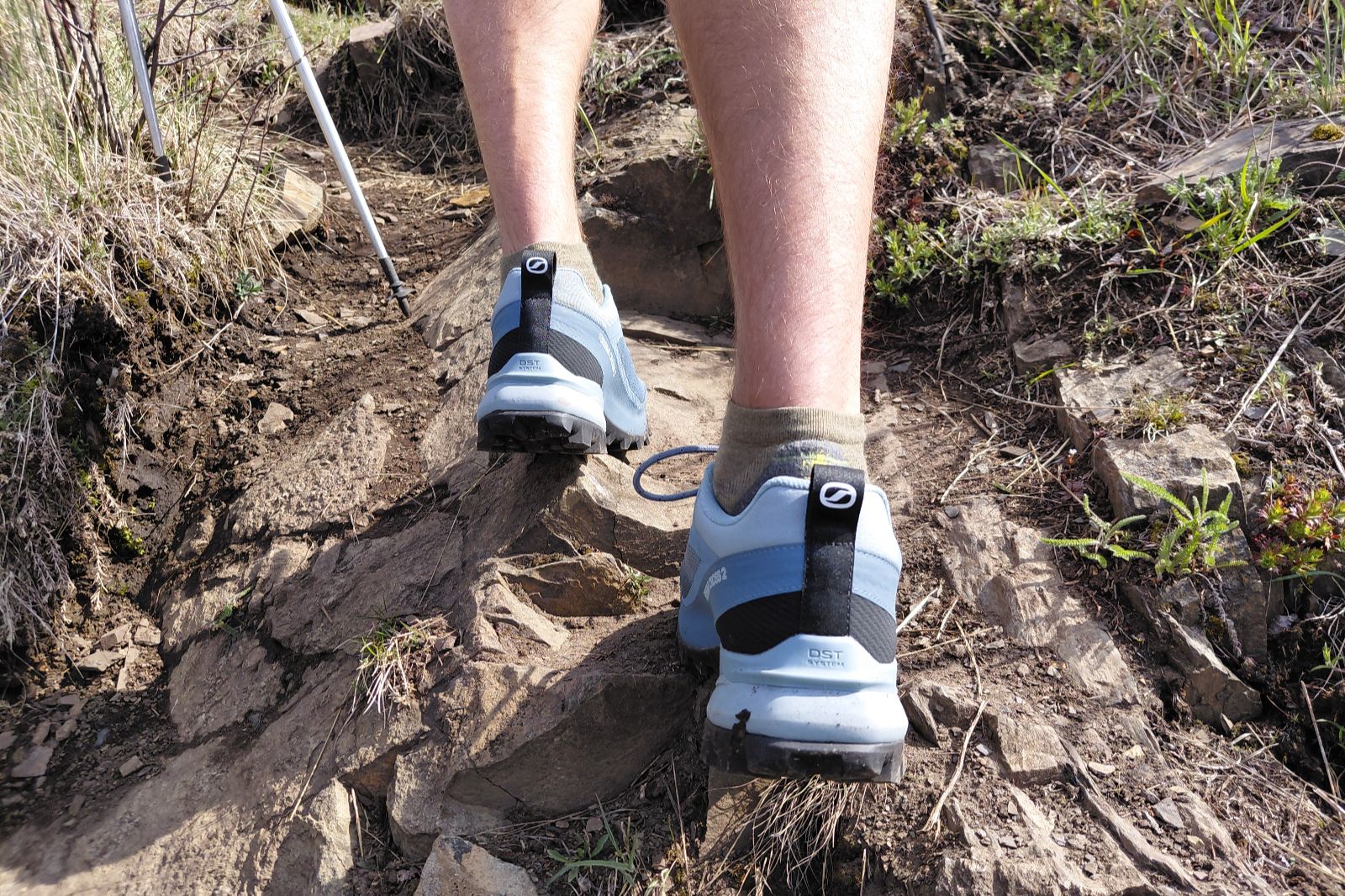 Close-up of a person's feet wearing light blue hiking shoes on a rocky trail.