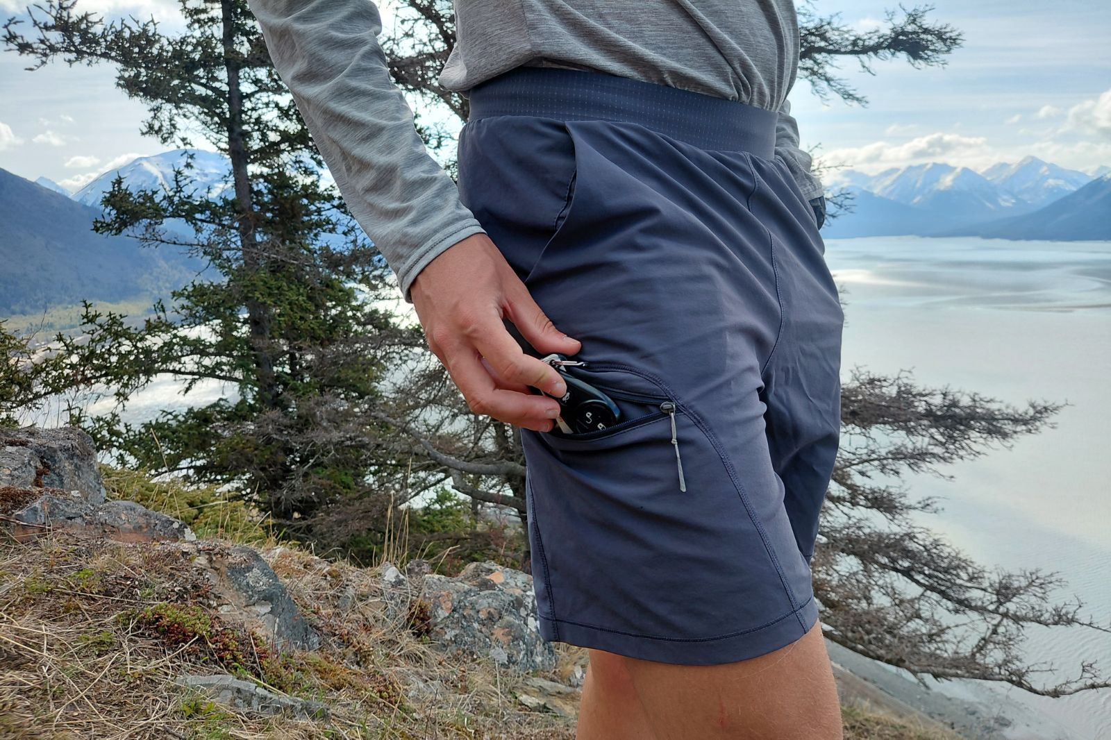 A close-up side view of a person standing on a rocky trail overlooking the ocean while wearing dark blue shorts.