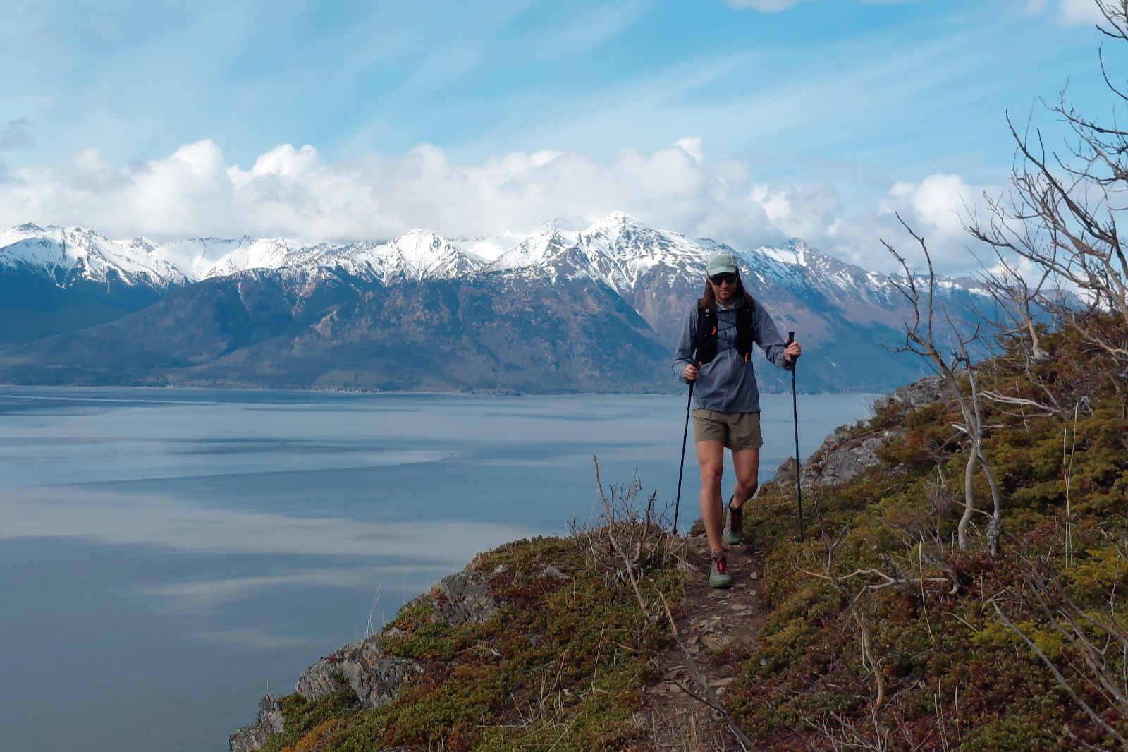 A man walks along a narrow path with snowcapped mountains in the background.