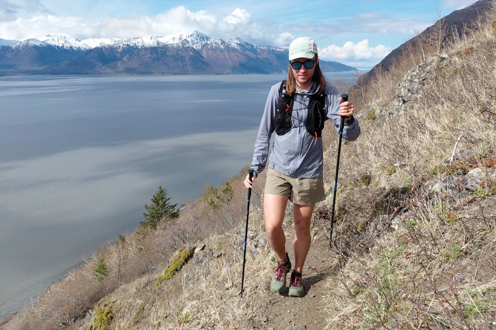 A man walks up a trail with trekking poles and the ocean in the background.
