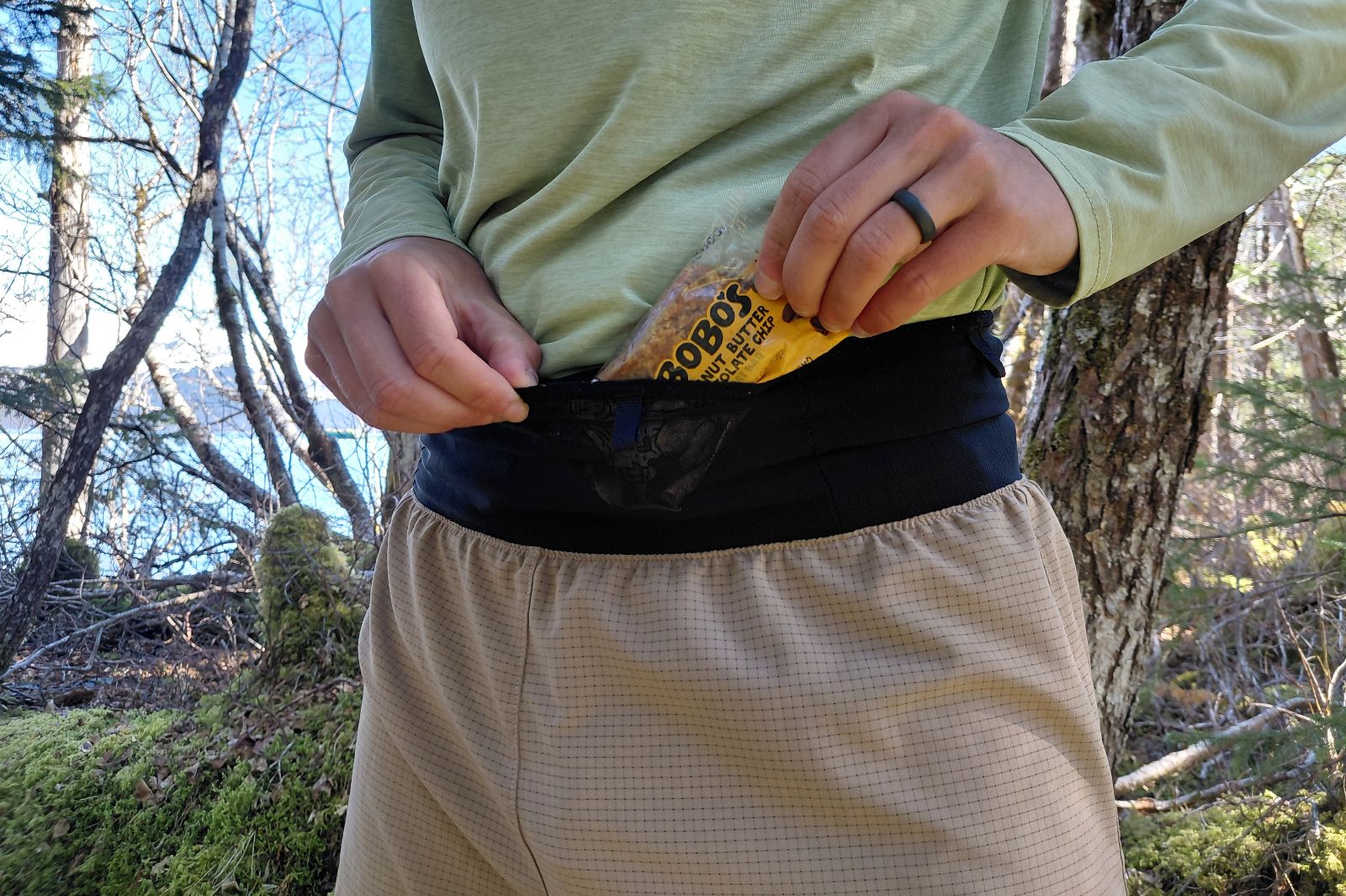 A close-up view of a person adjusting a black hip pack or waistband while wearing a green technical shirt.