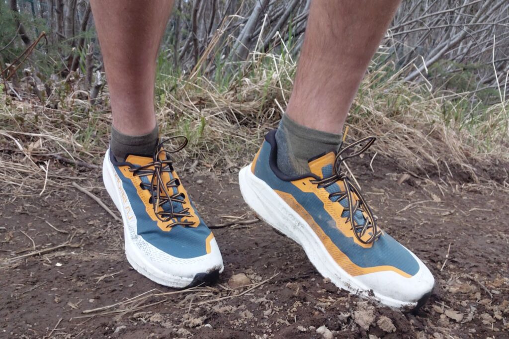 Person wearing blue and orange running shoes on a dirt path.