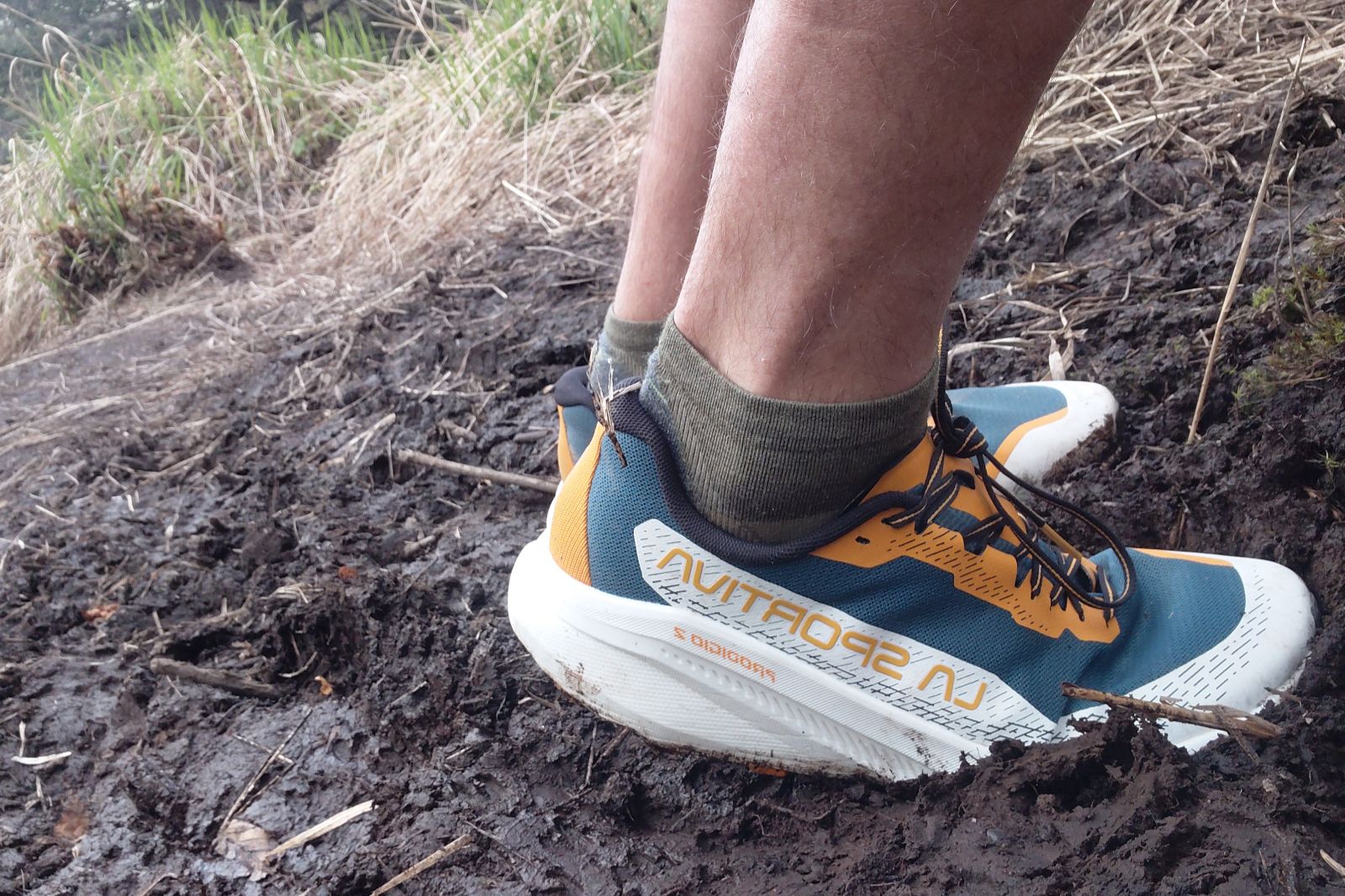 Close-up of a person in running shoes walking through mud on a trail.