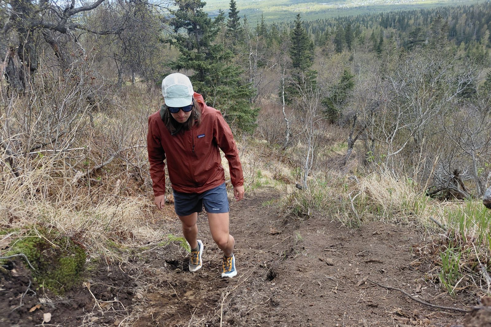 Person hiking up a dirt trail on a hillside, surrounded by dry grass and trees.