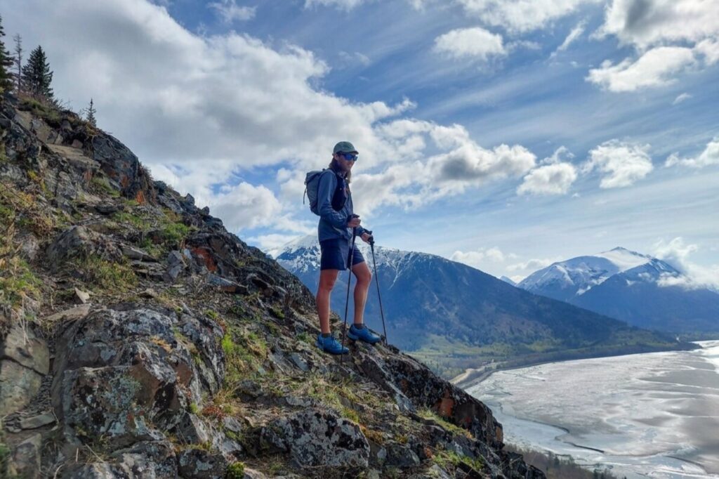 A hiker walks along a steep trail with an expansive view of a large body of water and a forested shoreline.