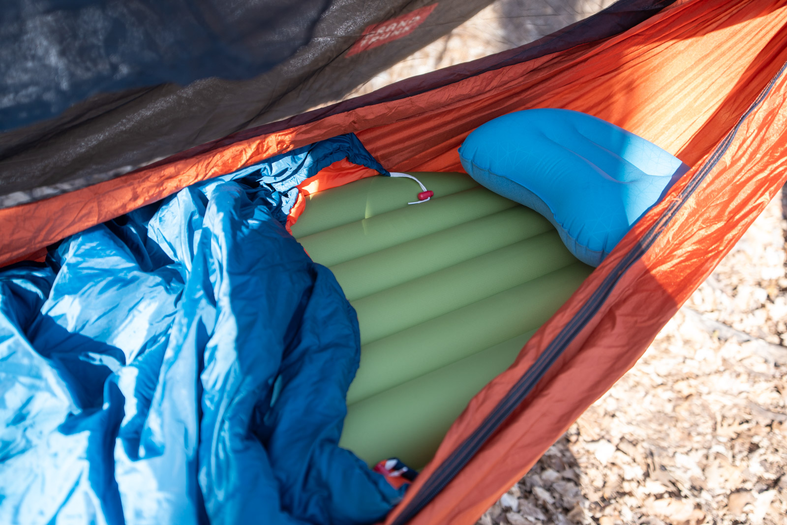 A sleeping bag, sleeping pad, and pillow are inside of an orange hammock.