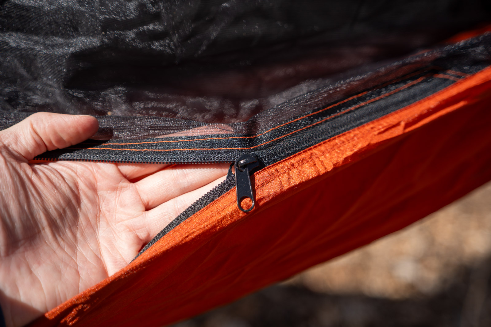 A hand holds up a zipper on a hammock.