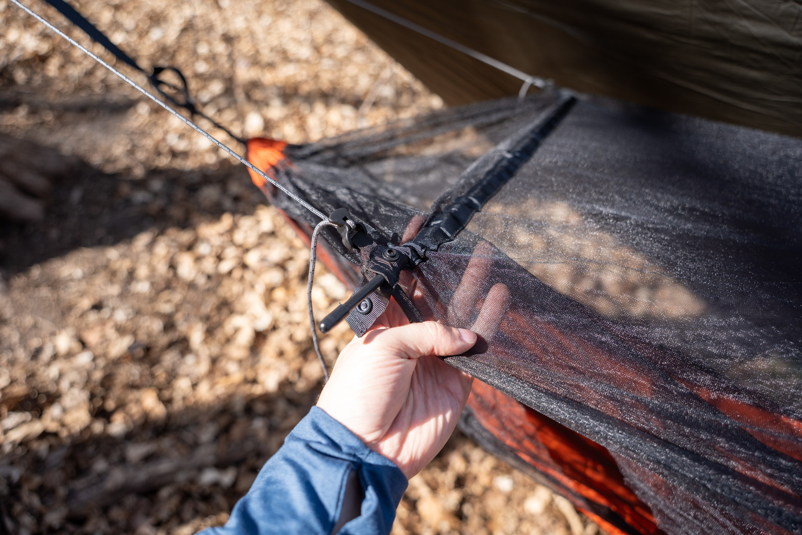 A hand holds a hammock bug net with a spreader bar inserted into a sleeve.