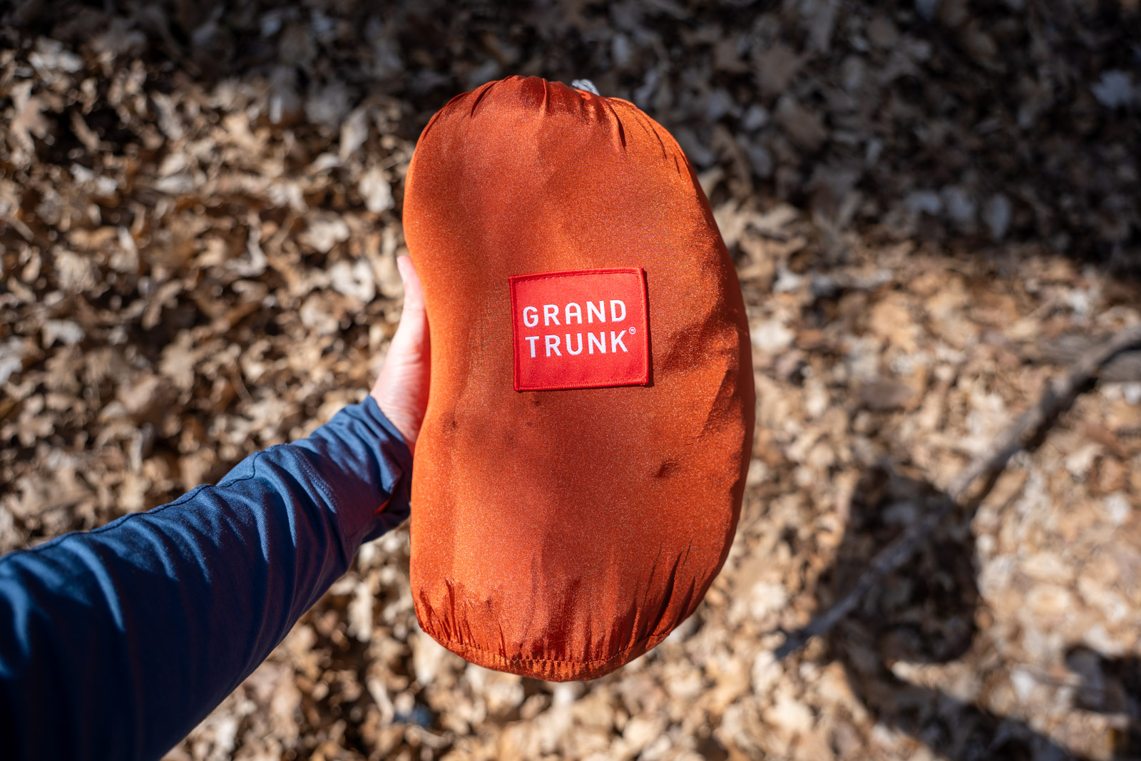 A hand holds out a full orange stuff sack.