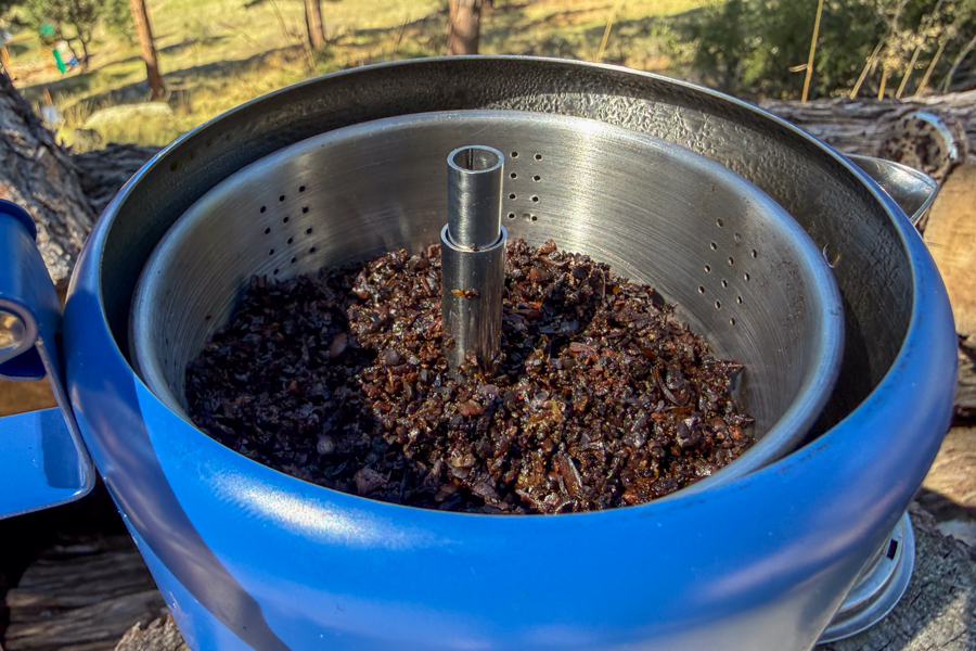 Close-up image of an open coffee percolator showing the used coffee grounds in the basket after brewing.