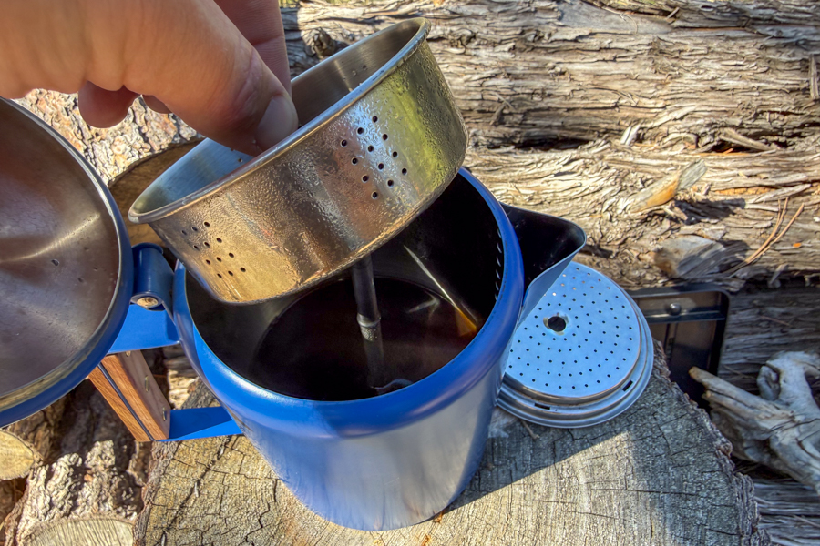 A coffee percolator basket being lifted out of the pot after brewing to show the internal setup.
