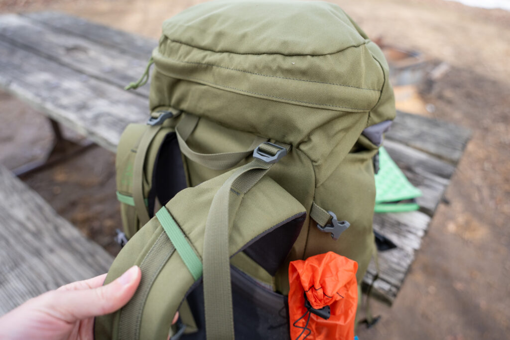 A hand holds shoulder straps on a green backpack