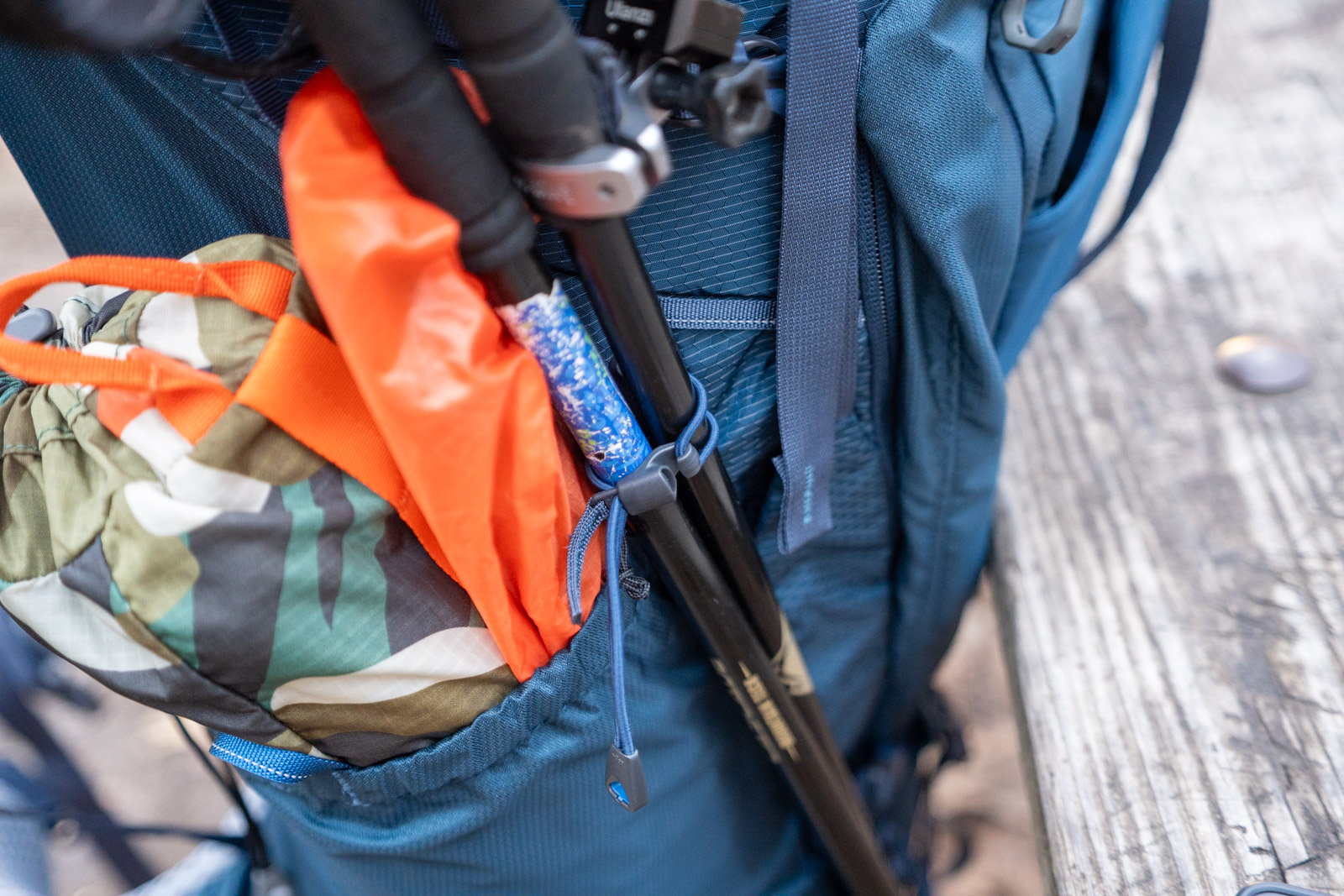 Trekking poles are stashed on the side of a backpack and secured with an elastic cord