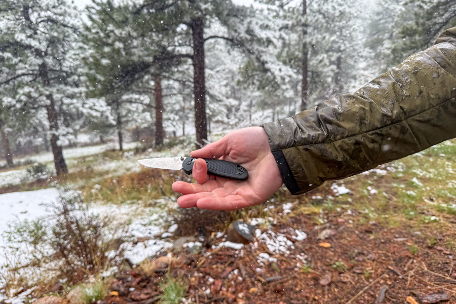 Mini Griptilian 556 hecho en banco sostenido abierto en una mano durante la caída de nieve en un campamento húmedo.
