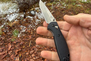 Benchmade Mini Griptilian 556 open in hand outdoors with wet ground and light snow around the campsite.