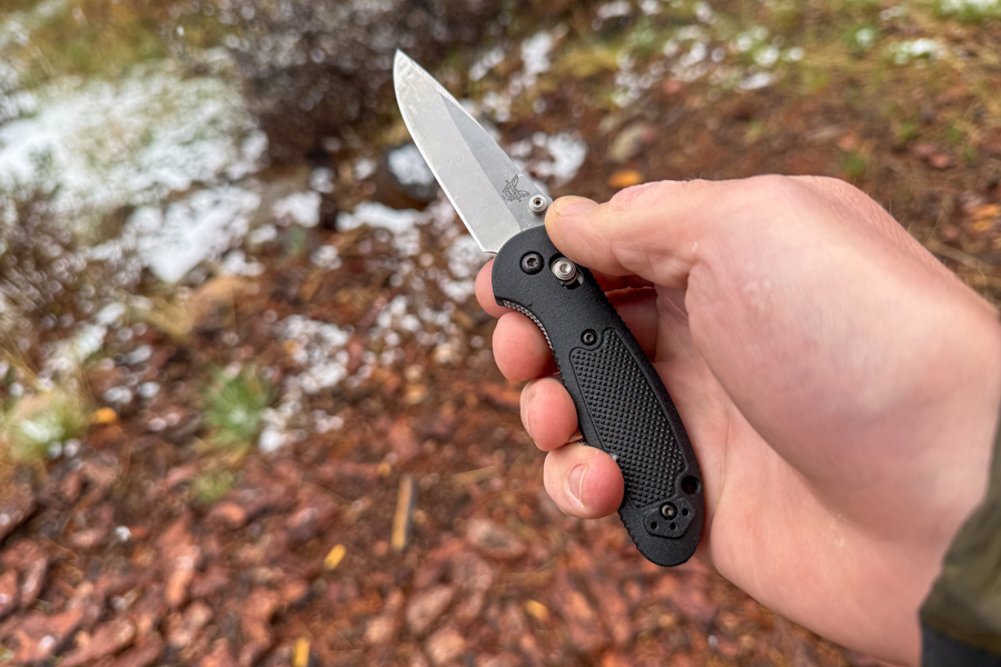 Mini Griptilian 556 hecho en banco, sostenido con una mano al aire libre, mostrando el mango compacto y el tamaño de la hoja.