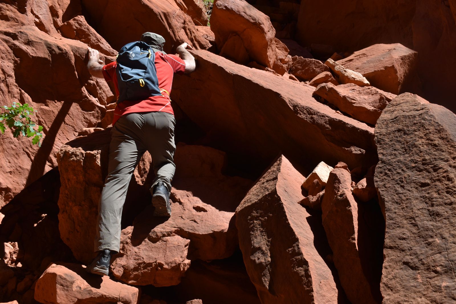 A hiker climbs up red rock boulders with the Black Diamond Pursuit 15 daypack on his back.