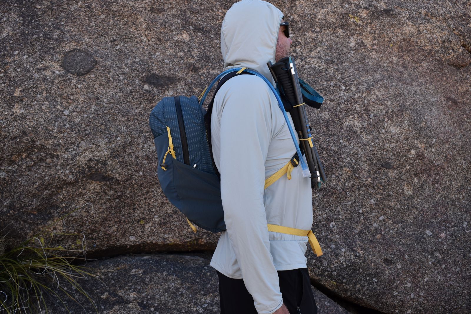 Profile view of a male hiker in the Black Diamond Pursuit 15 with trekking poles attaches to his shoulder straps