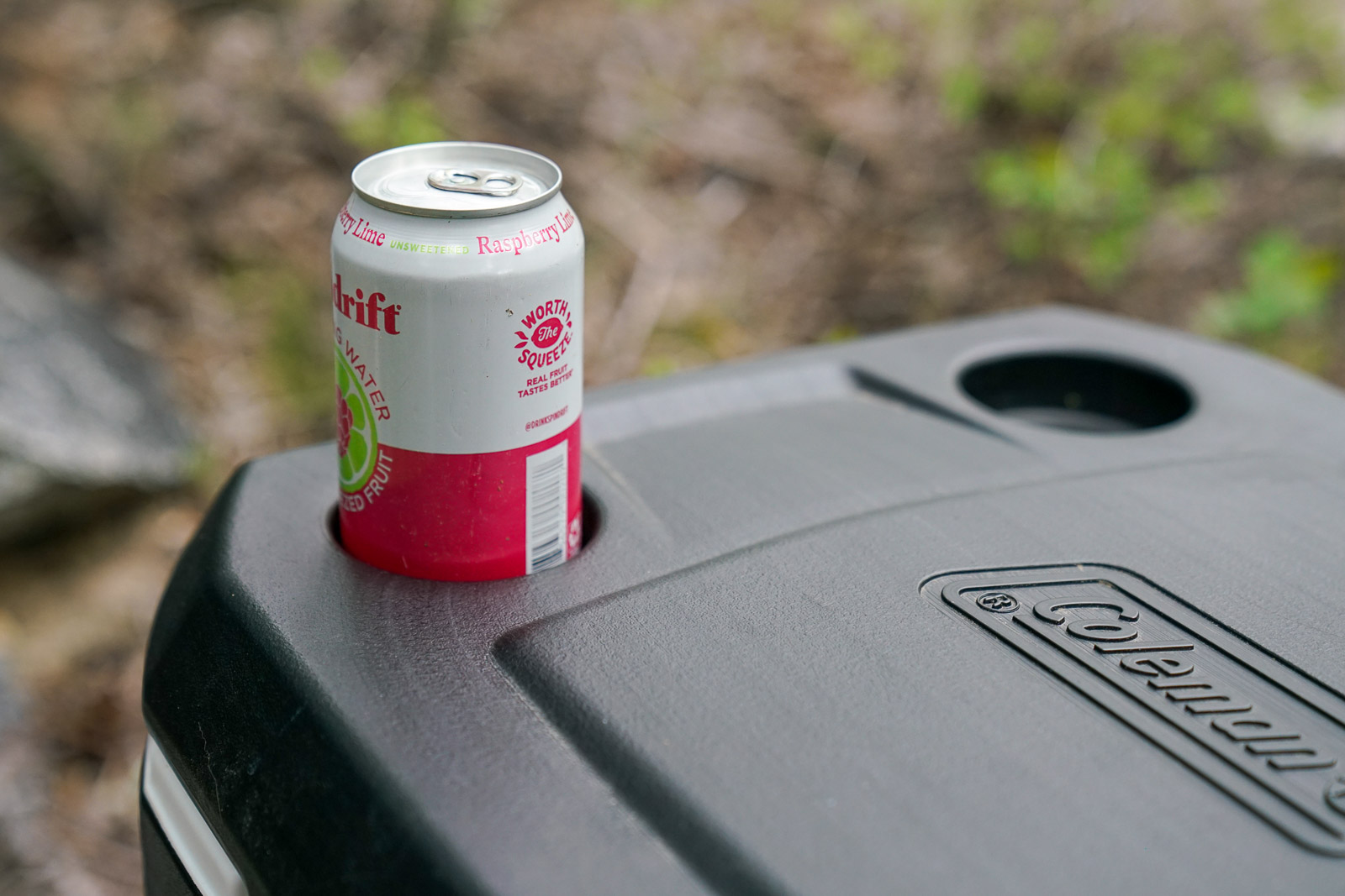 A canned beverage sits in the built-in cupholder on a cooler lid.