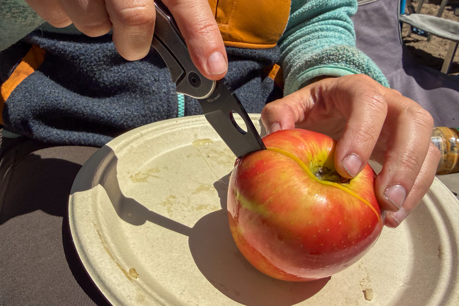 Coast Contra knife being used to slice into an apple on a paper plate during camp lunch.