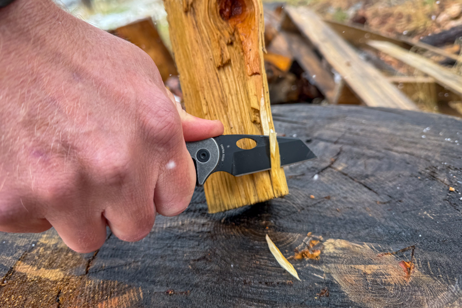 Coast Contra knife being used to shave a thin curl from a piece of split wood on a tree stump.