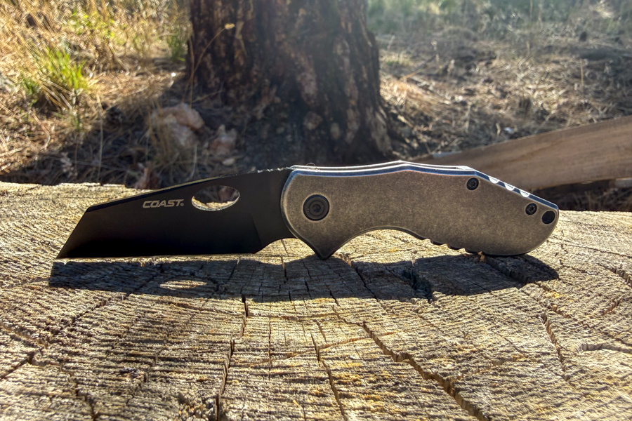 Side view of the open Coast Contra knife resting on a sunlit tree stump.