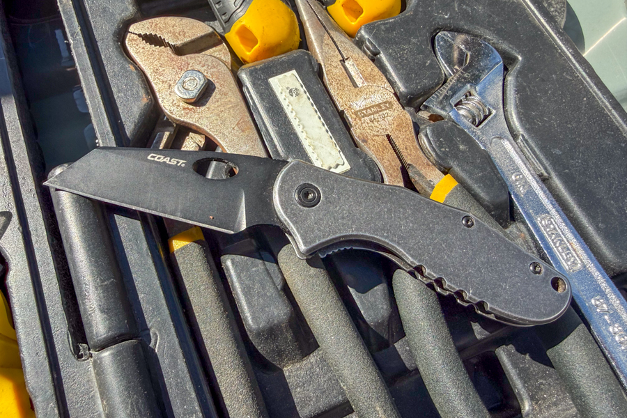 Coast Contra knife open and resting in a toolbox among hand tools.