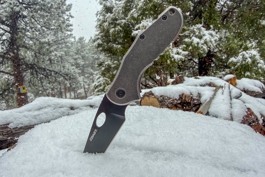 Coast Contra knife stuck blade-first into fresh snow with snowy forest in the background.