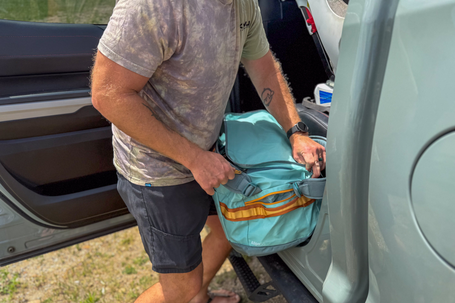 Person loading the Cotopaxi Allpa Getaway 55L into the back seat of a vehicle.