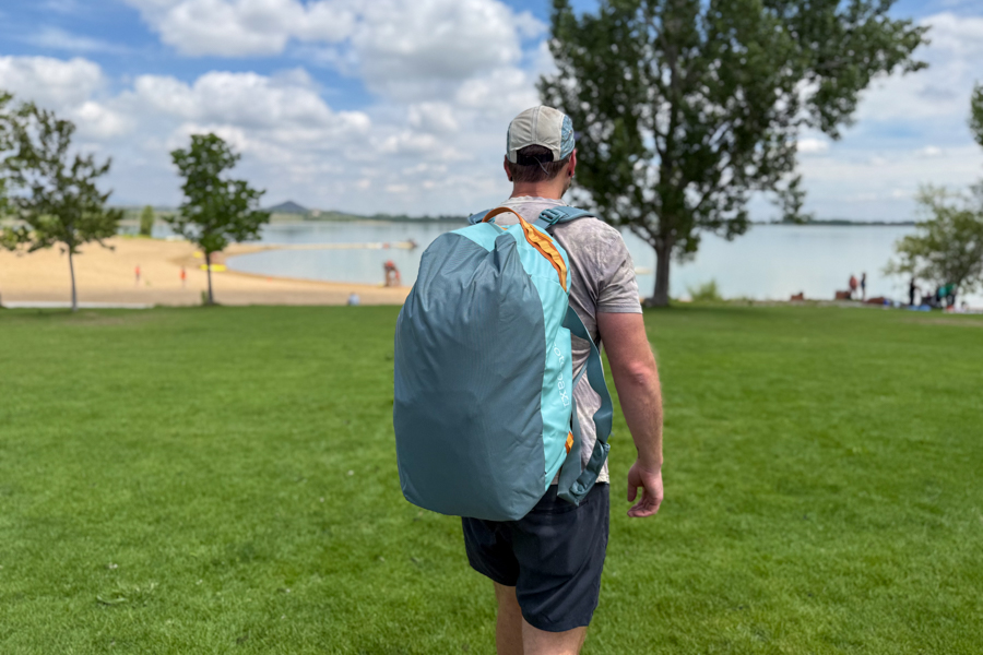 Person wearing the Cotopaxi Allpa Getaway 55L as a backpack while walking across grass near a lake.