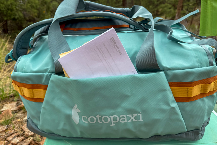 Cotopaxi Allpa Getaway 55L duffel showing the front stash pocket with papers tucked behind the tote handles.