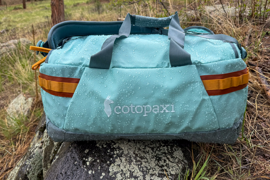 Cotopaxi Allpa Getaway 55L covered in water droplets on a rock during weather-resistance testing.