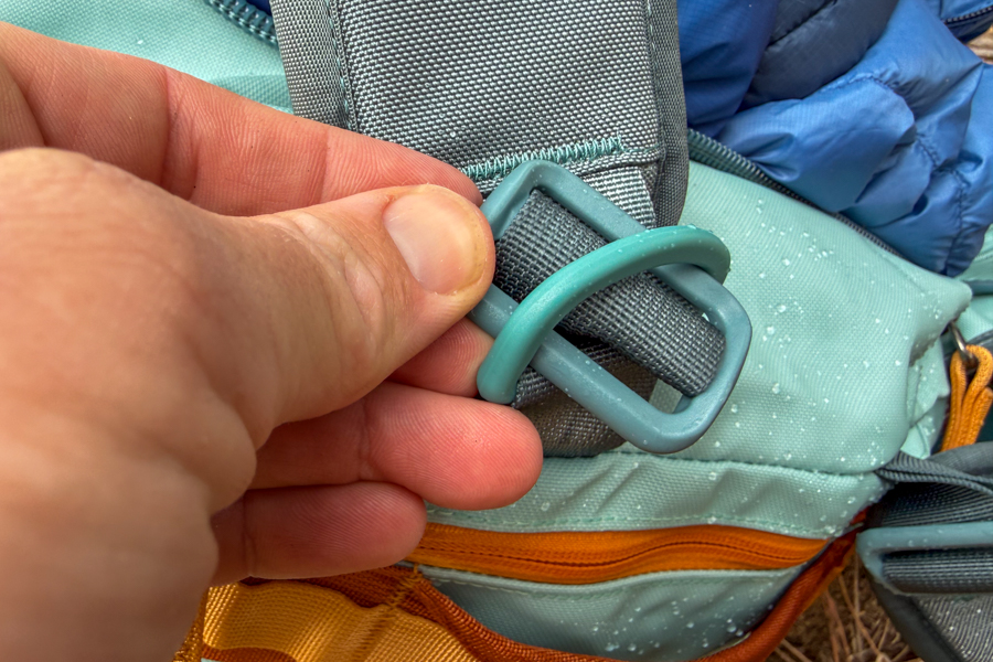 Close-up of the Cotopaxi Allpa Getaway 55L backpack strap buckle and webbing with water droplets on the bag.