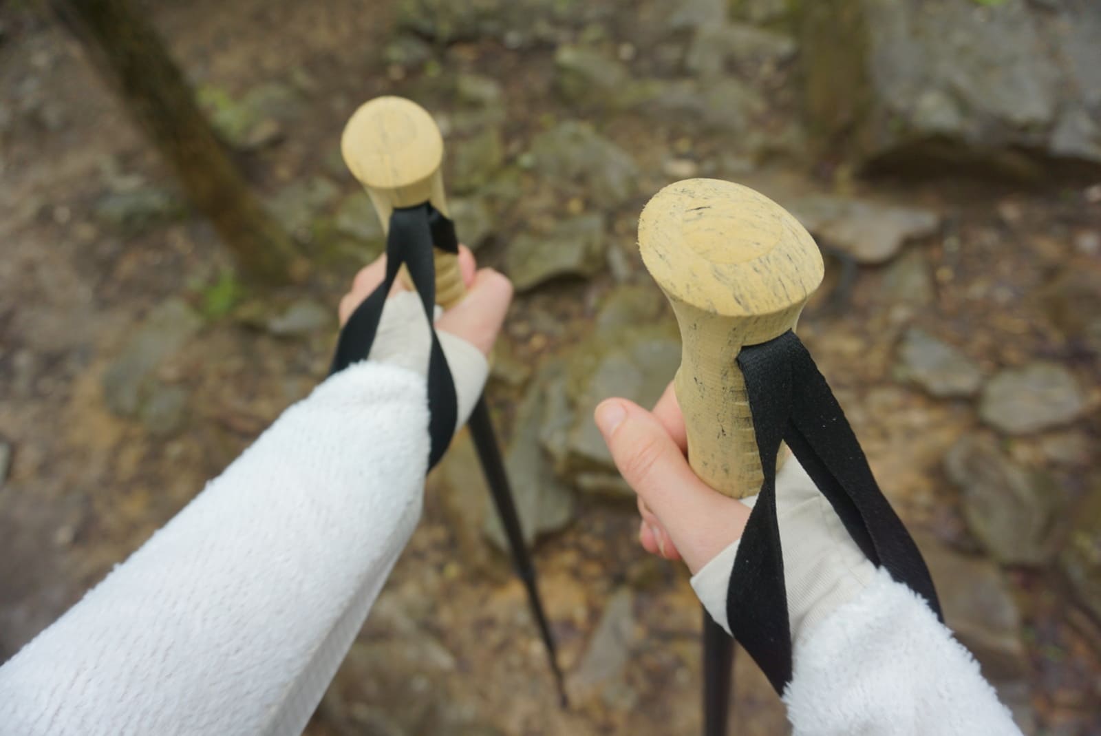 Woman holds trekking poles with jacket over hands.