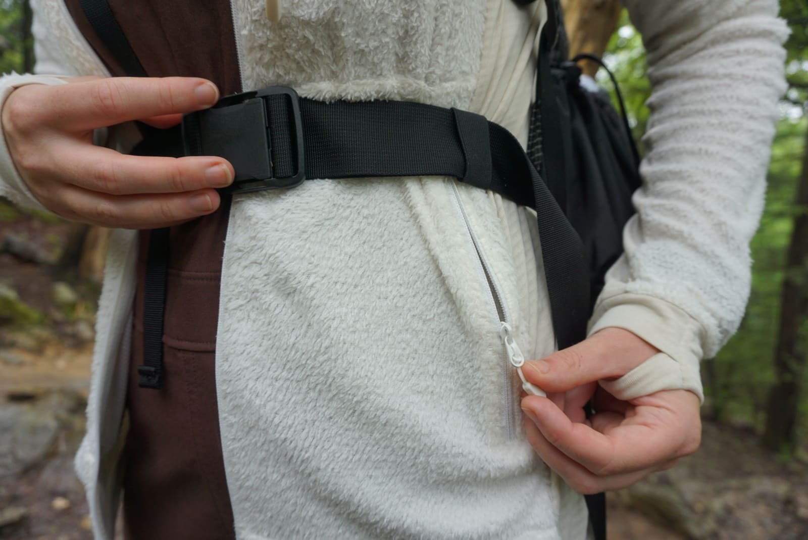 Woman unzips hip pocket of jacket while wearing a pack with a hipbelt