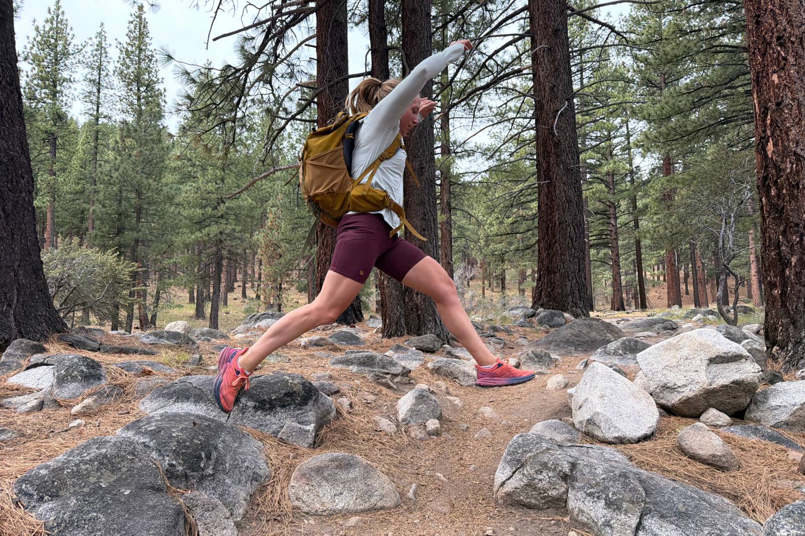A woman jumps from one boulder to another across the trail wearing a pair of thigh-length hiking shorts.