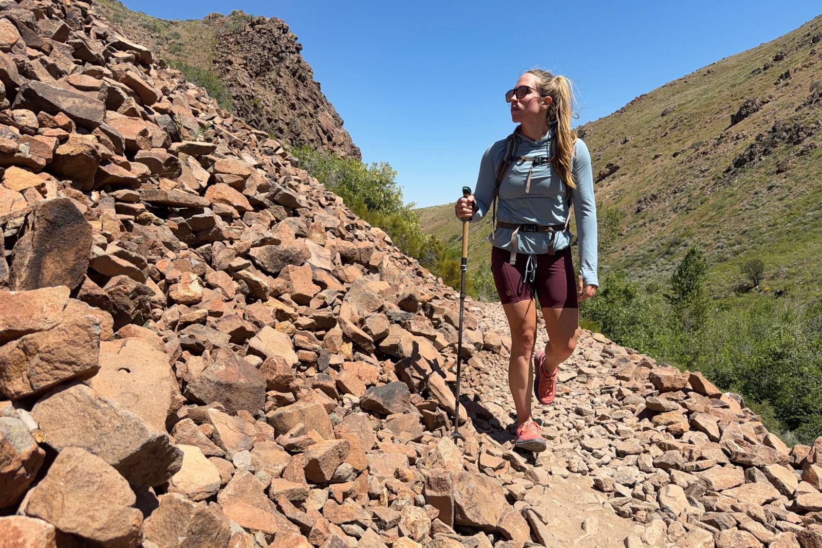 A woman hikes toward the camera on a rocky trail wearing a pair of thigh-length hiking shorts.