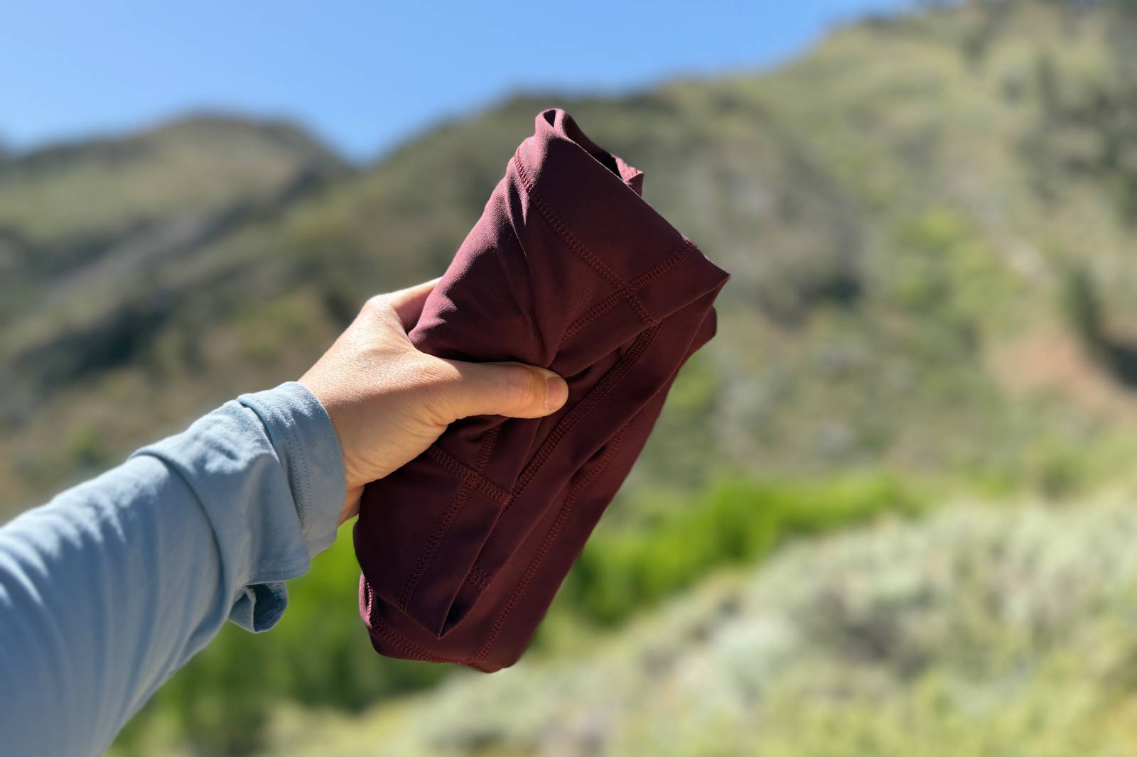 Close-up image of a woman's hand outstretched holding a pair of rolled-up hiking shorts.