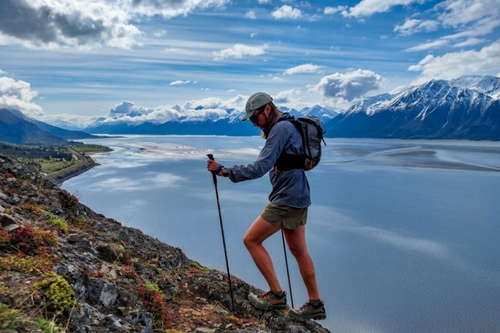 A man walks up a rocky ridgeline with snowy mountains and the ocean in the distance.