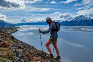 A man walks up a rocky ridgeline with snowy mountains and the ocean in the distance.